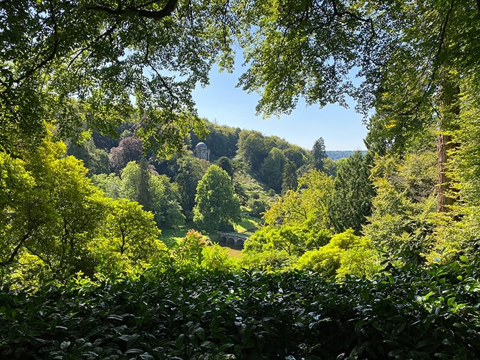 view through trees to temple of apollo folly in stourhead gardens